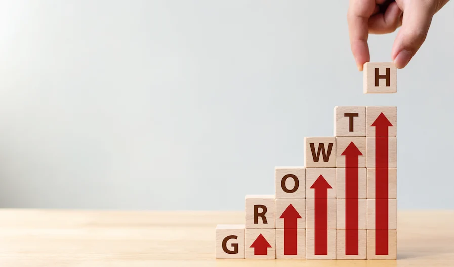 Rockefeller Habits: Hand placing a wooden block with the letter 'H' on top of stacked blocks spelling 'GROWTH' with red arrows pointing upwards.