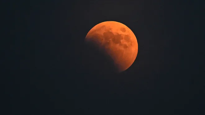 Partially eclipsed moon with a reddish hue, known as a blood moon, with Earth's shadow visible on the lower left.