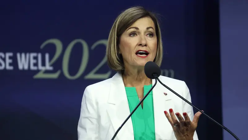 Iowa Gov. Kim Reynolds speaking at the RISE WELL 2020 event, wearing a white blazer over a green top.
