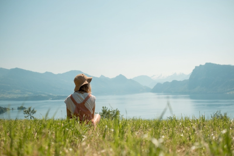 Woman in hat sitting on grass, looking at lake and mountains, symbolizing new beginnings after probation.