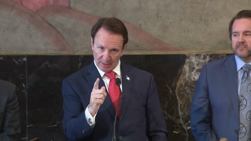 Jeff Landry speaks at podium, pointing for emphasis, navy suit and red tie.