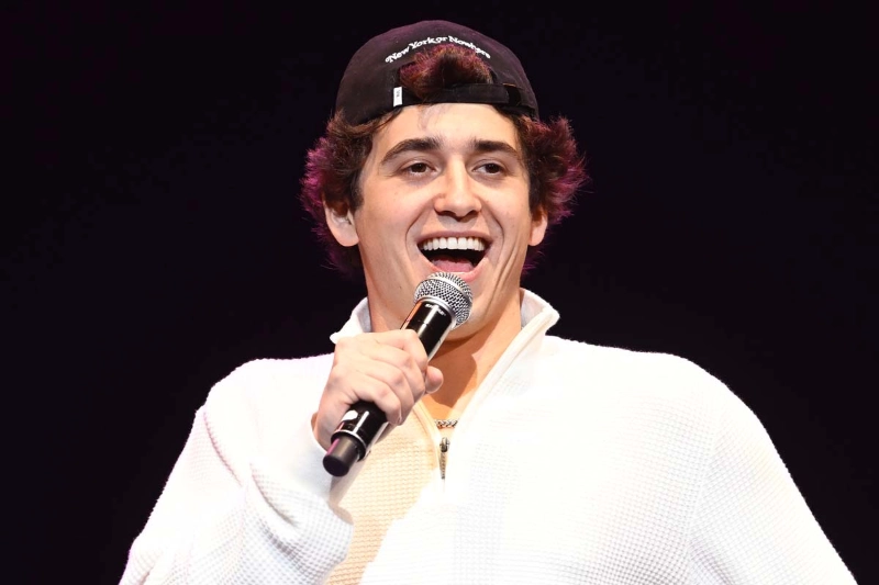 Marcello Hernandez in white shirt and cap, holding a mic on stage.