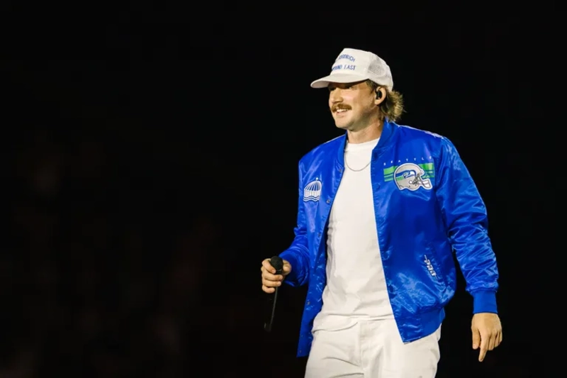 Morgan Wallen in blue jacket singing on stage, 2026 tour, black background, Image Credits: Saskia Potter