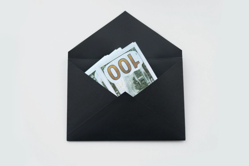 Black envelope with $100 US bills inside, symbolizing financial rewards. Image Credits: Photo by Hanna Pad / Pexels