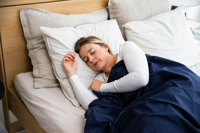 Woman peacefully sleeping in bed with soft white and navy sheets. Image credits: Slaapwijsheid.nl / UNSPLASH