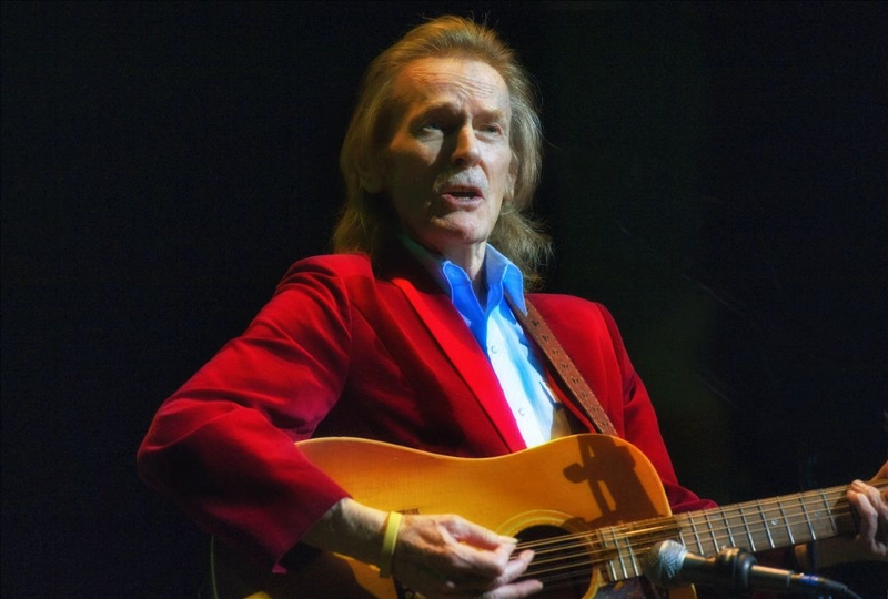 Gordon Lightfoot in red jacket performing live with acoustic guitar on stage. Credits: Gordon Lightfoot