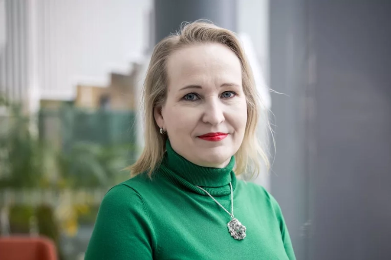 Minna Helle, Finnish labor market expert, smiles in a green turtleneck with decorative pendant. Image Credits - Karoliina Vuorenmäki