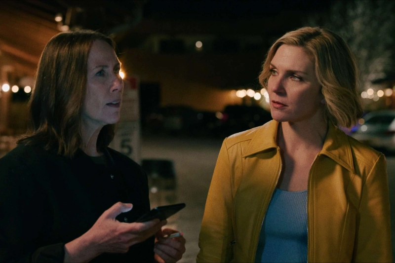 Pluribus series duo at night, woman in yellow jacket, friend holding phone, image credits: Apple TV+