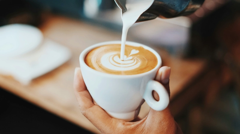 What is a latte being poured, hand holding cup, image credits: Fahmi Fakhrudin / UNSPLASH