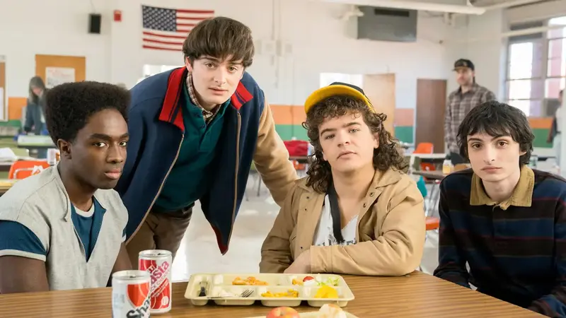 Stranger things cast: Lucas Sinclair, Will Byers, Dustin Henderson, Mike Wheeler in Hawkins High cafeteria.