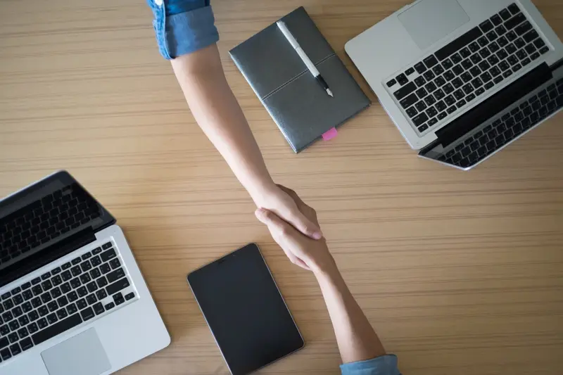Business agreement represented by two people shaking hands over a table, highlighting the March 2025 U.S. Jobs Report.