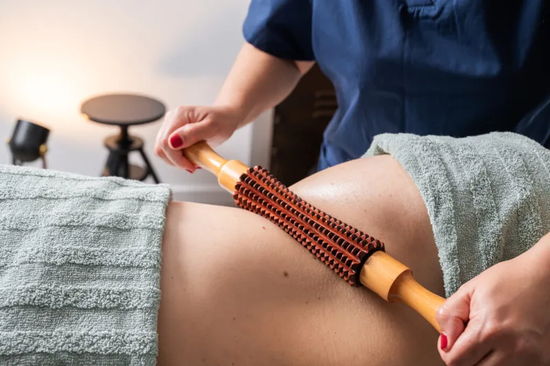 Benefits of Wood Therapy: therapist using wooden roller on thigh.