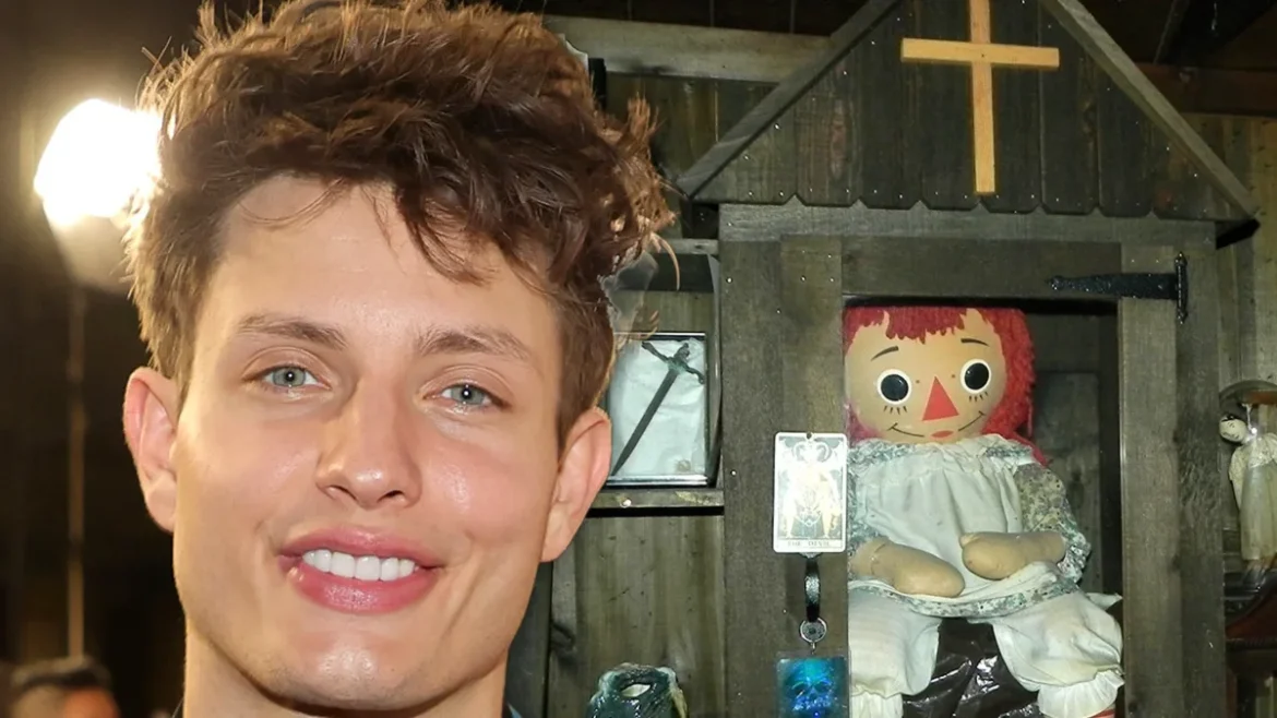 Matt Rife: smiling with Annabelle doll in wooden case, close-up.