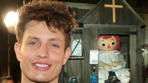 Matt Rife: smiling with Annabelle doll in wooden case, close-up.