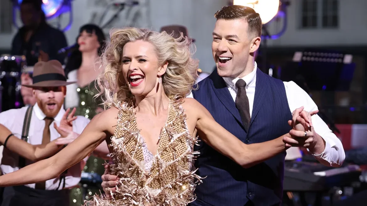 Glamorous couple dancing on stage, man in suit, woman in gold dress, BBC ballroom show. Image credits: BBC