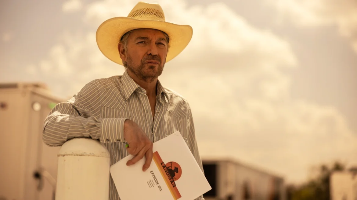 Man in a striped shirt and cowboy hat holds a 'Landman' production script outdoors on set. Image Credits - Paramount+