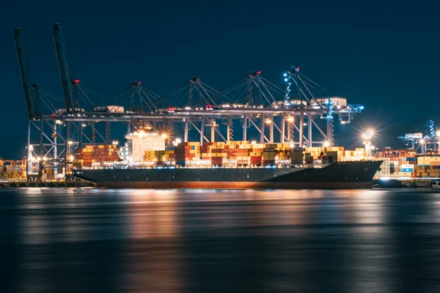 A container ship loaded with cargo under lit cranes at a port at night