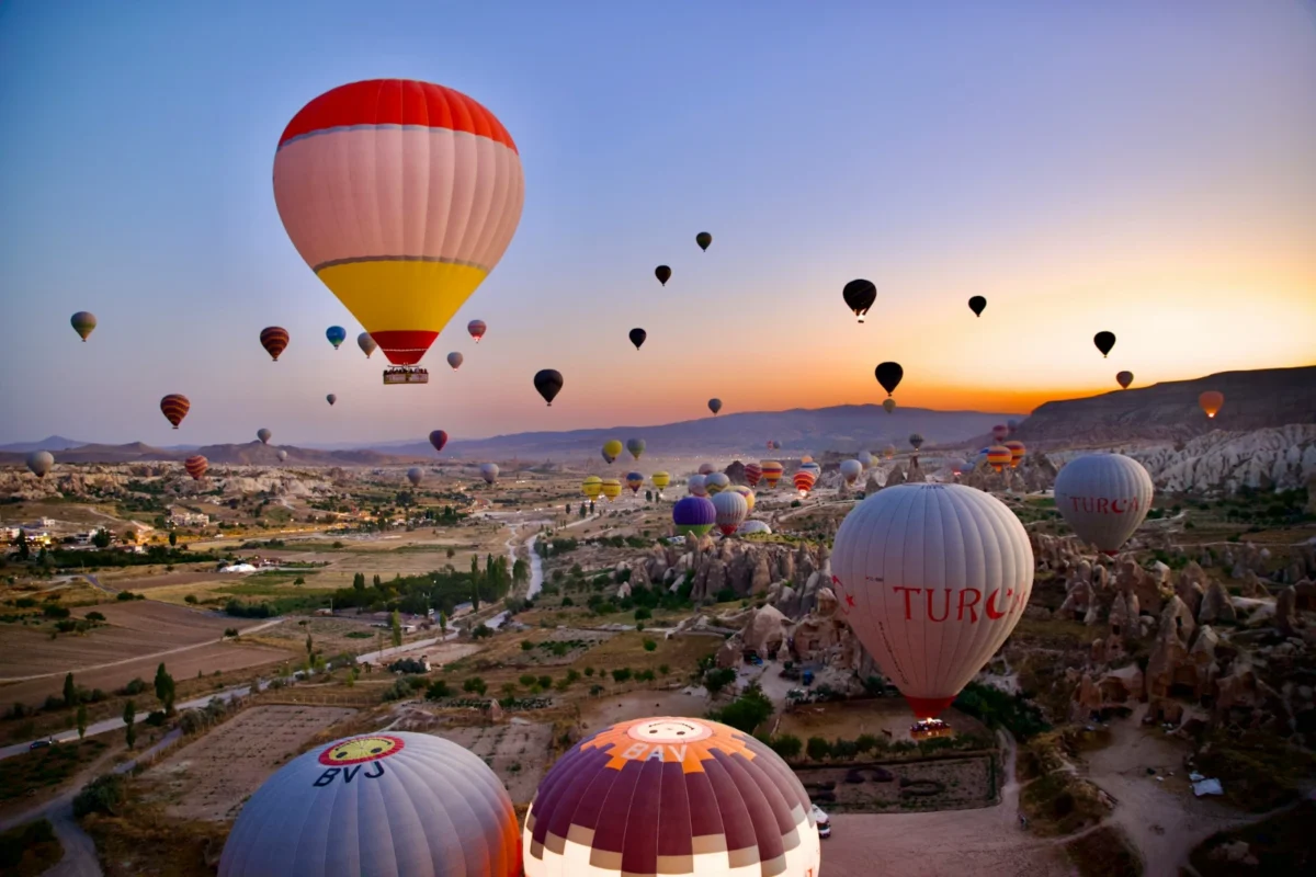 Hot air balloons rising at sunrise over the rock formations of Cappadocia, Türkiye