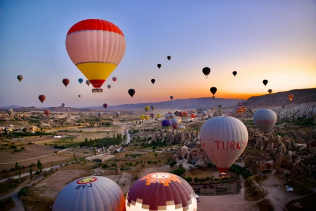 Hot air balloons rising at sunrise over the rock formations of Cappadocia, Türkiye